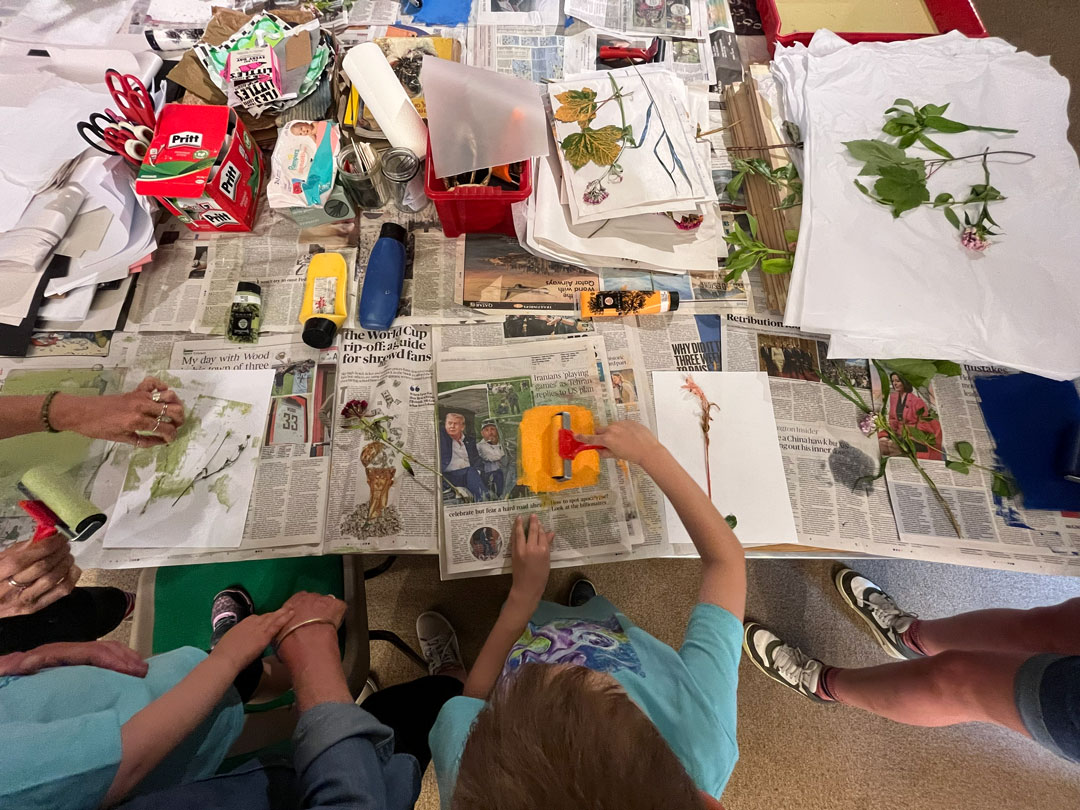 A birds eye view of a small child using a paint roller to apply paint to a leaf.