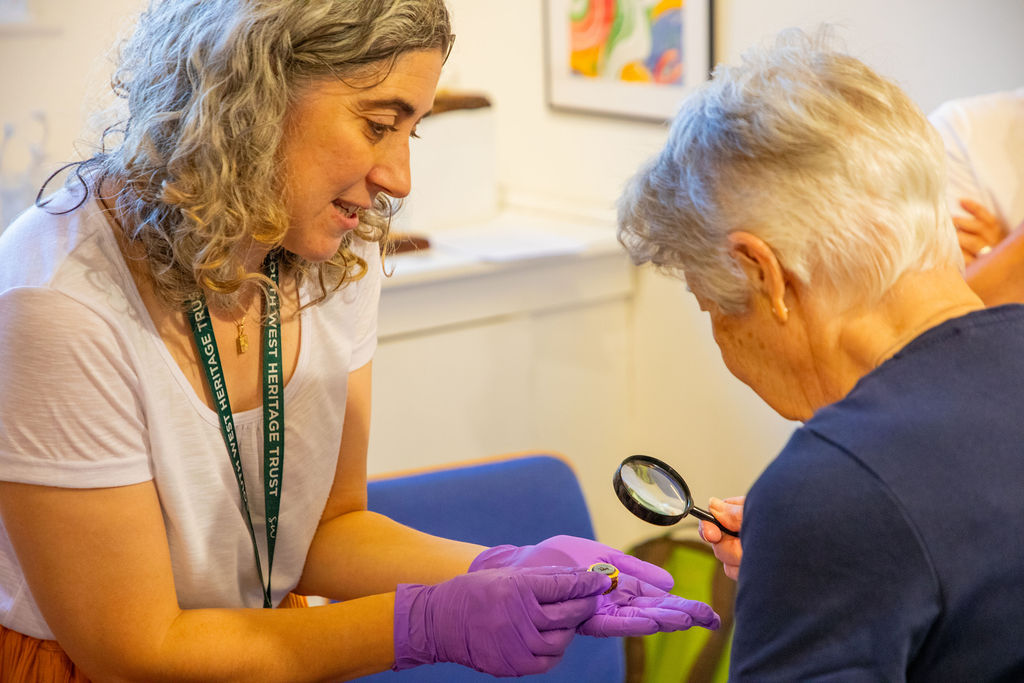 A Museum Curator showing an elderly woman an ornate golden Roman ring through a magnifying glass.