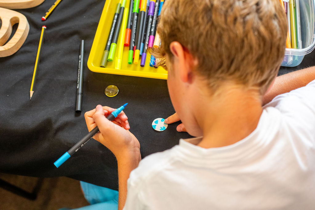 A young boy drawing onto a small paper disc to go in a ring he created.