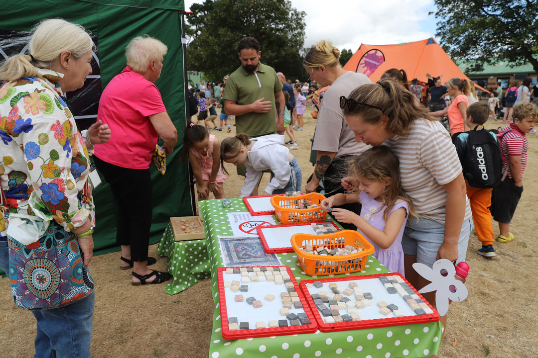 A group of children and adults gathered around an outdoor table with Roman Mosaic themed activities.